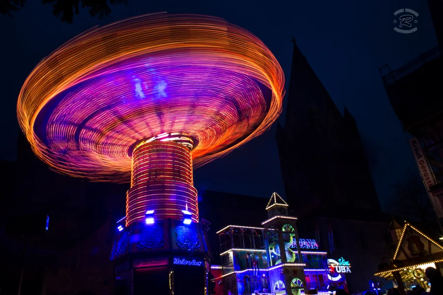 Ein beleuchtetes Kettenkarussell bildet kreisförmige violette und orange Lichtspuren