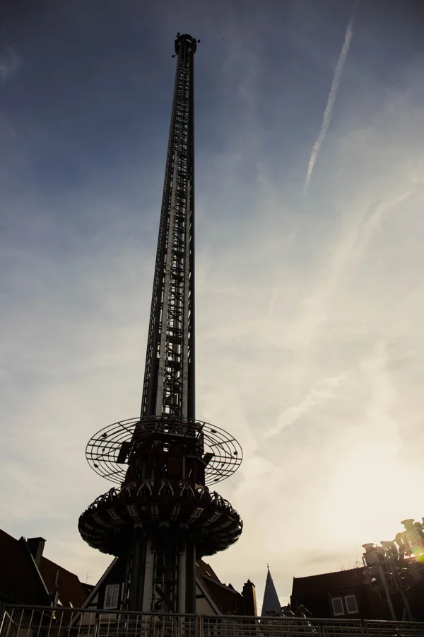 Ein hoher schlanker Turm eines Fahrgeschäfts vor einem hellen Abendhimmel