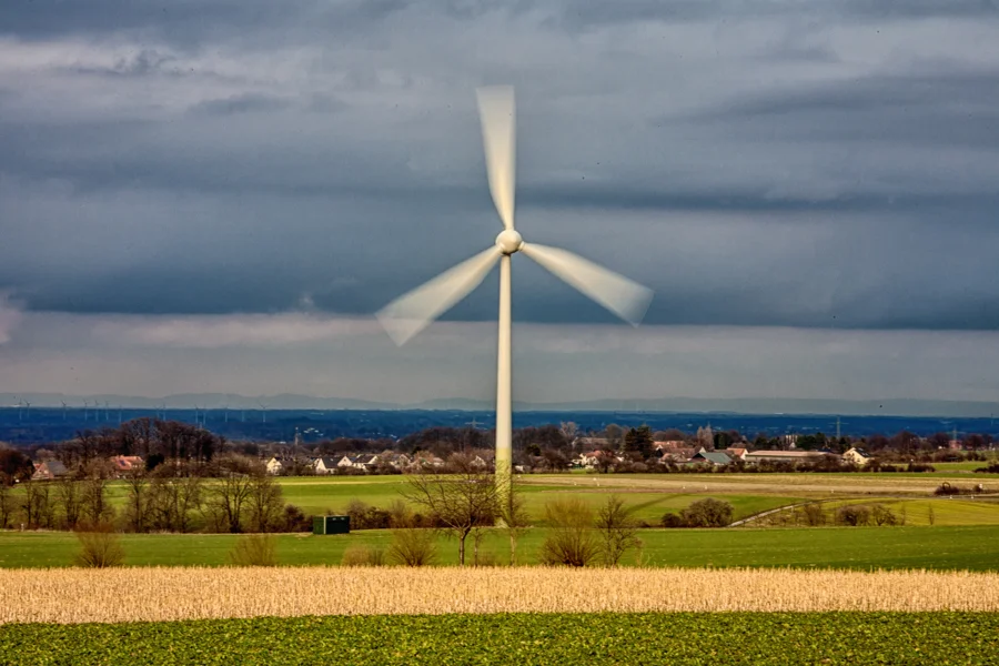Einzelnes Windrad vor dunklen Wolken über einem gelben Feld